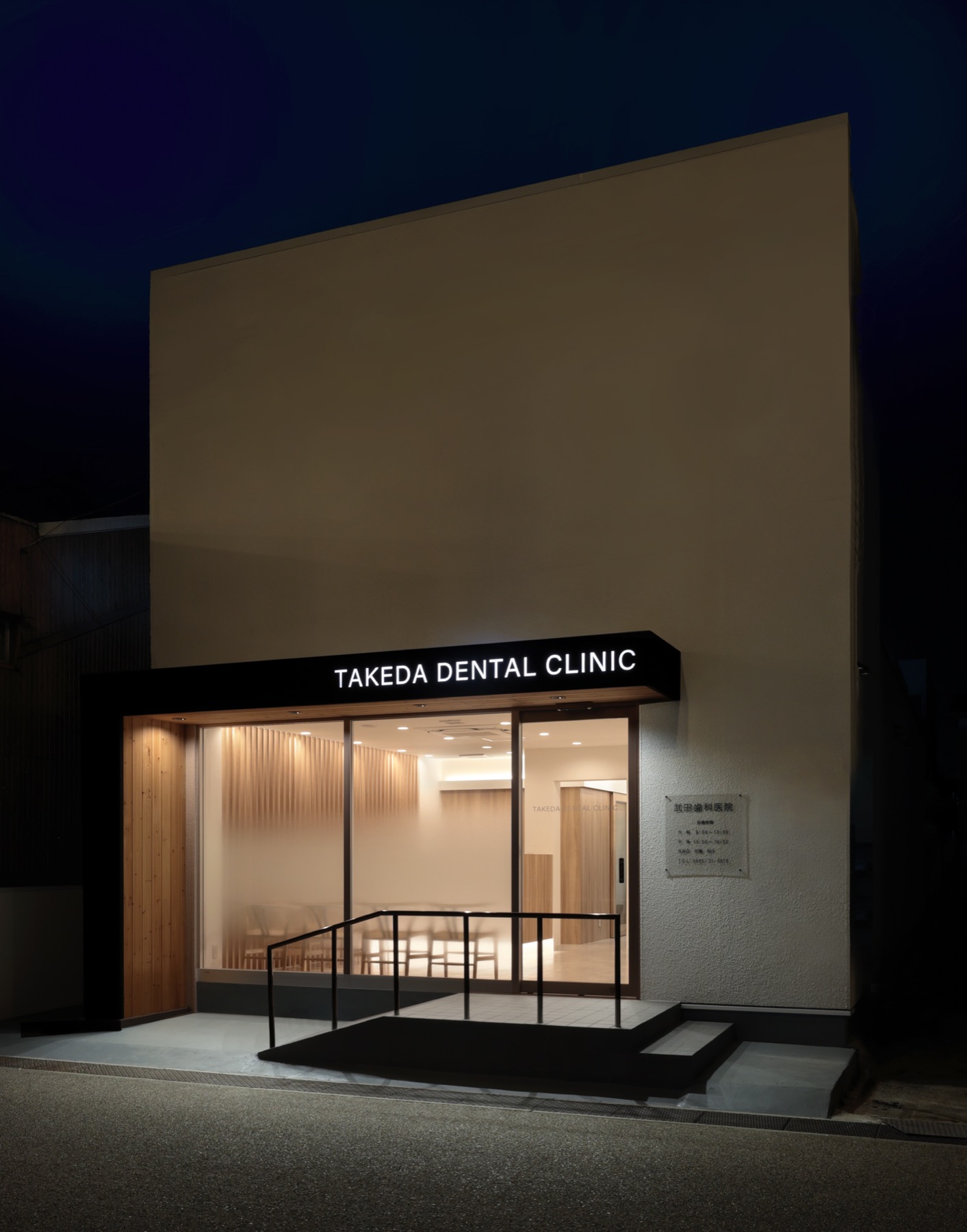 夜の医院の外観。灯りの入った待合の窓と、入口の上の看板